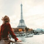 Femme debout au bord de la Seine près de la Tour Eiffel, vue emblématique de Paris, silhouette en manteau rouge au coucher du soleil. intégrant le sens de « meilleur arrondissement de paris pour vivre » dans une description naturelle.