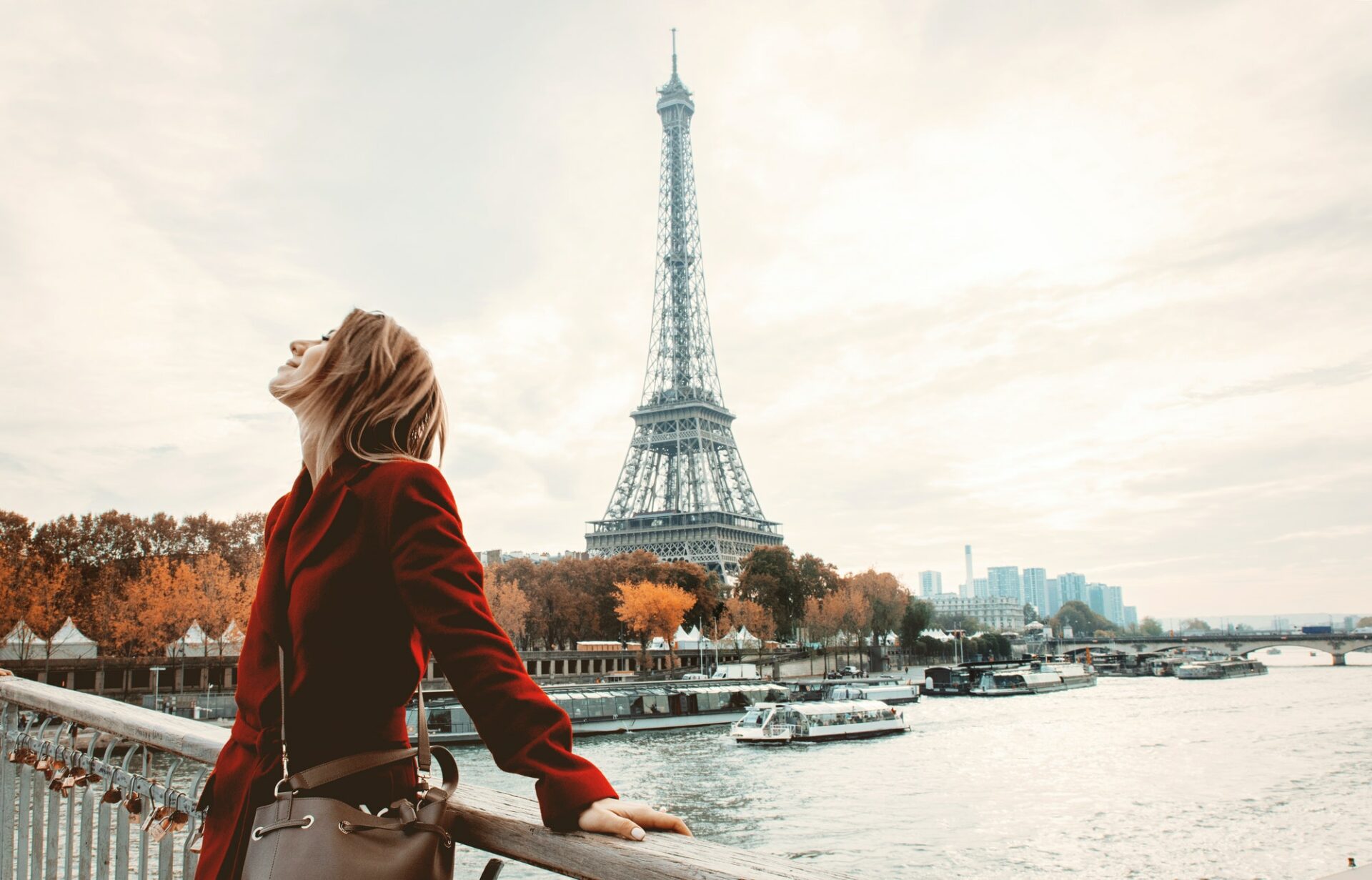 Femme debout au bord de la Seine près de la Tour Eiffel, vue emblématique de Paris, silhouette en manteau rouge au coucher du soleil. intégrant le sens de « meilleur arrondissement de paris pour vivre » dans une description naturelle.