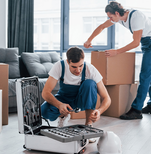Two hommes en tenue de travail montent une boîte à outils et préparent des emballages dans un intérieur avec des cartons, près d’un garde-meuble paris.