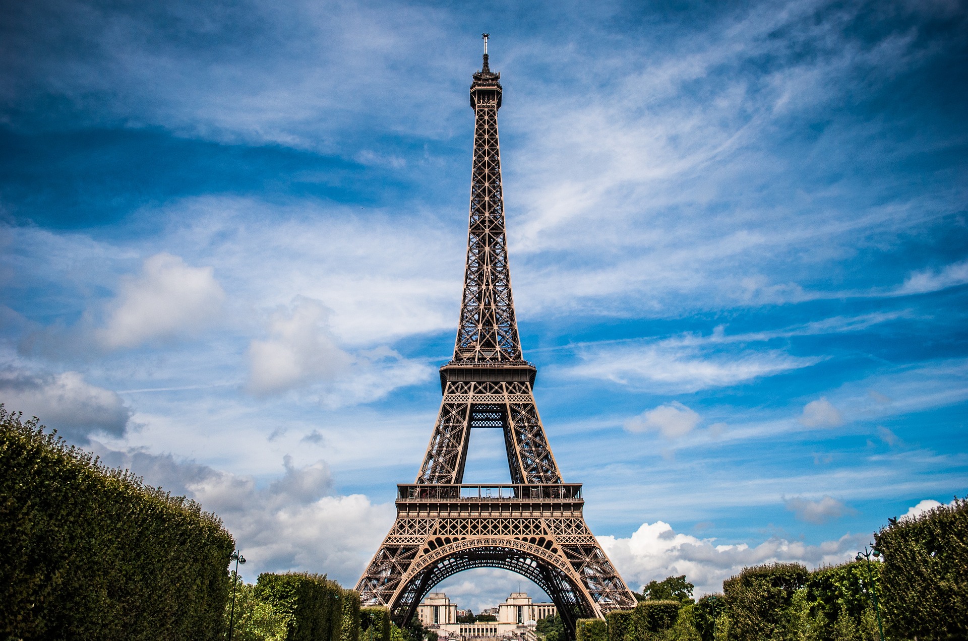 La tour Eiffel vue au centre, entourée de jardins et d’un ciel bleu avec quelques nuages.
